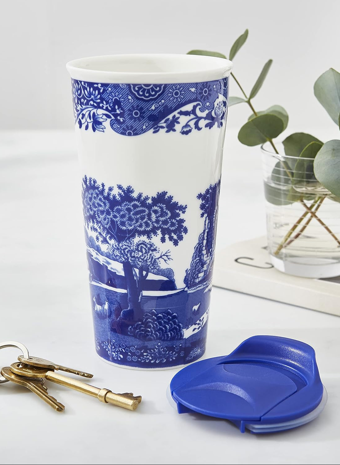 Blue and white patterned travel Mug with a matching lid on a surface with keys and a plant.